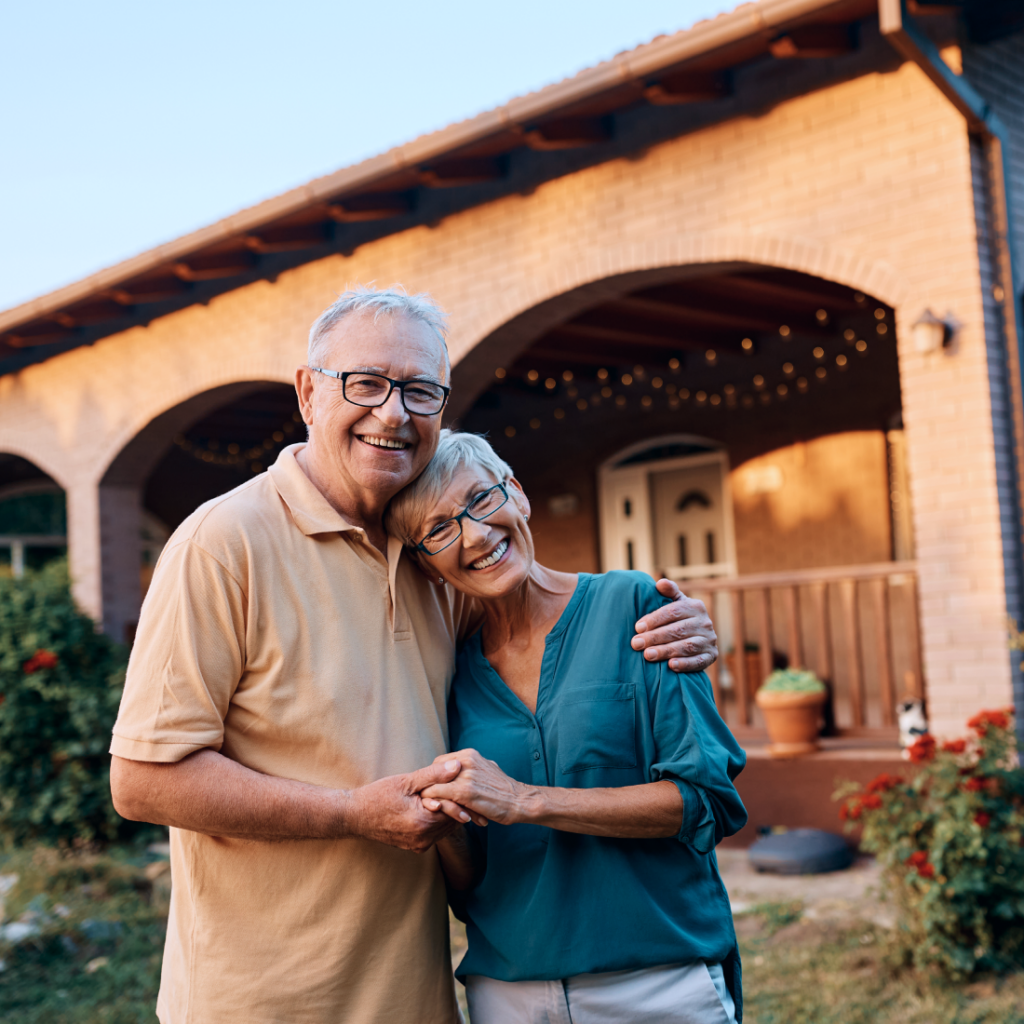 Cheerful senior couple standing together in front of their home, smiling warmly